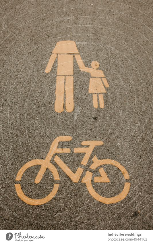 A bicycle lane sign and a pedestrian walkway sign on the tarmac. Yellow paint, black road. The head of the pedestrian is missing. Urban road mark. bike symbol