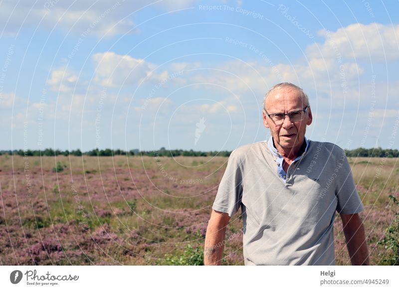 Portrait of a male senior citizen, in the background blooming heath landscape and blue sky with clouds Human being Man Senior citizen portrait Skeptical Looking