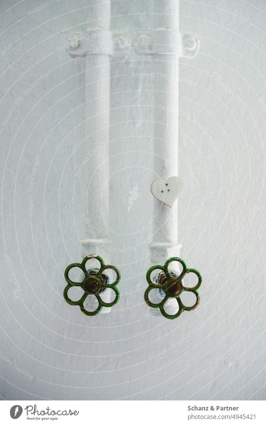 two white painted water pipes with green rotary valves and a white heart in front of a white wall Warm water cold water installation Installer Heating Water