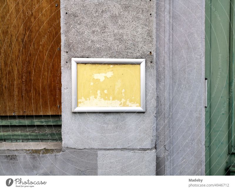 Neglected sign with yellow background and silver frame on gray concrete in the alleys of the old town of Bruges in West Flanders in Belgium Wall (building)
