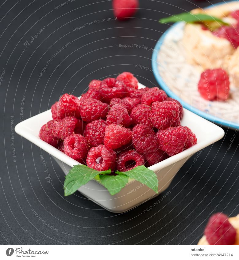 Ripe red raspberries in a white ceramic bowl on a black table berry raspberry raw ripe sweet tasty vegetarian vitamin whole wooden board eat food fresh
