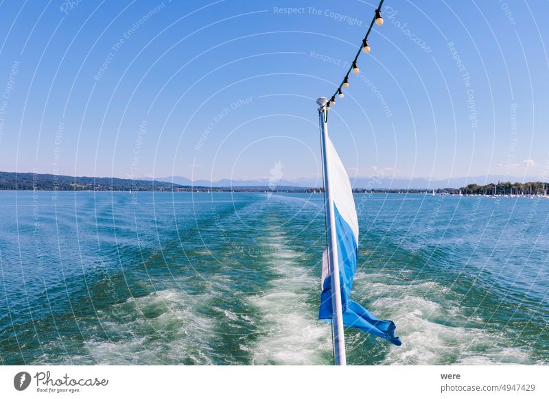View from a ship over the white and blue Bavarian flag over Ammersee lake in Bavaria with sailboats on the water and Ammergau Alps in the background Background