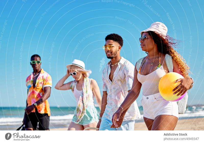 Happy diverse friends walking on beach smile summer weekend together sand happy blue sky resort daytime men glad women young delight stroll group cloudless sky