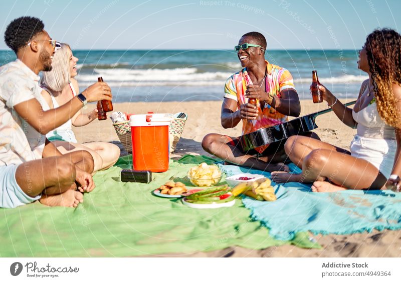 Diverse friends drinking beer and eating fruits beach picnic smile clink bottle happy weekend men women summer young diverse multiracial multiethnic black