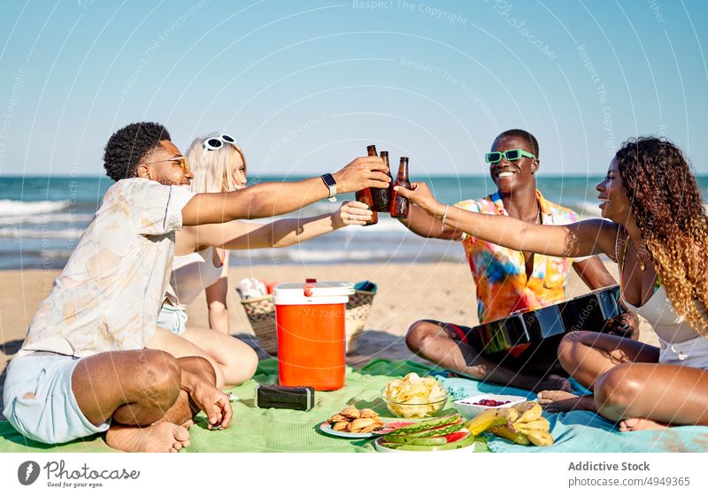 Diverse friends proposing toast on beach beer picnic smile clink bottle happy weekend men women summer young diverse multiracial multiethnic black