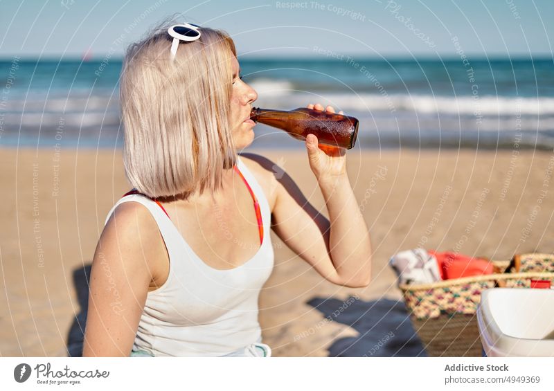Young woman drinking beer on beach weekend summer bottle alcohol picnic sip female young blond vacation sunglasses beverage holiday thirst sunlight shore season