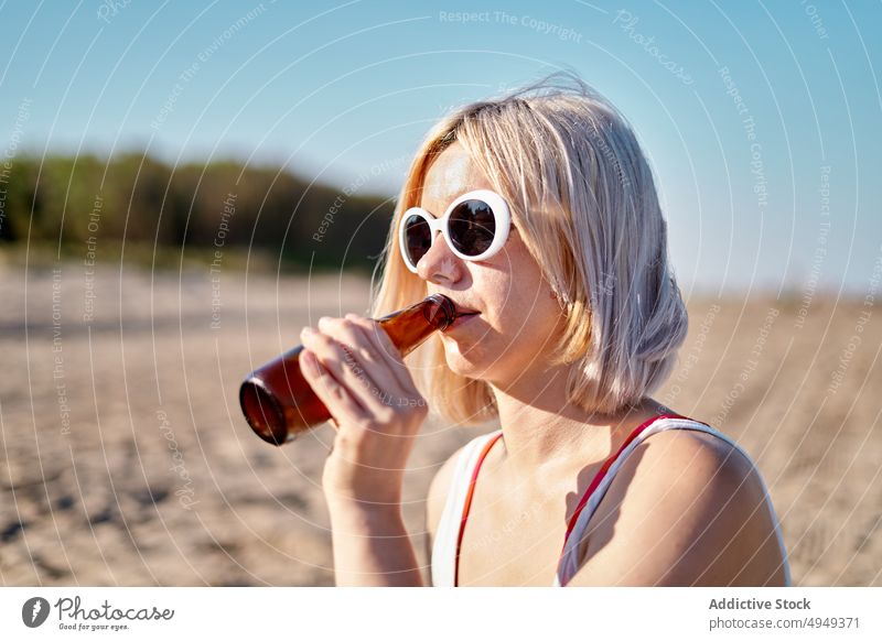 Young woman drinking beer on beach weekend summer bottle alcohol picnic sip female young blond vacation sunglasses beverage holiday thirst sunlight shore season