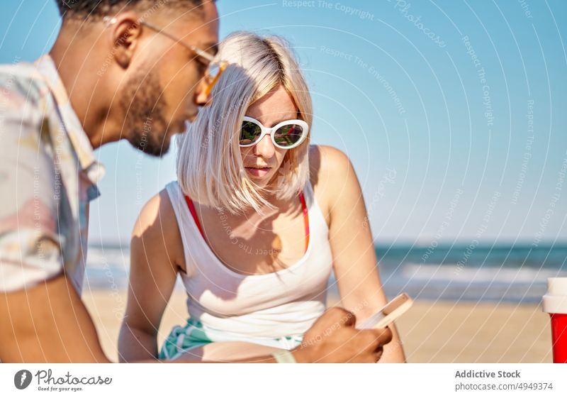 Diverse friends using smartphone on beach share sea together news scroll weekend man woman summer young diverse multiracial multiethnic black african american