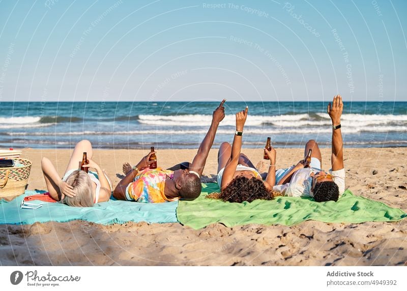 Young diverse best friends lying on seashore and drinking beer people beach vacation relax point up holiday spend time communicate together young multiracial
