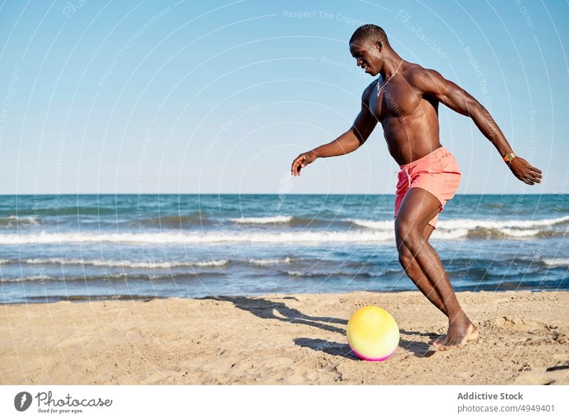 Black man kicking ball on beach sea play smile having fun energy summer male black african american ethnic happy sand shirtless vacation barefoot ocean holiday