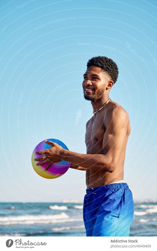 Glad black male with ball near sea man smile beach weekend blue sky vacation summer happy african american ethnic cheerful positive shore coast holiday ocean