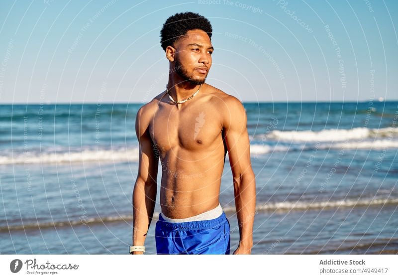 Black young male tourist standing near sea man beach summer weekend curly hair resort vacation thoughtful holiday portrait coast shore tourism activity water