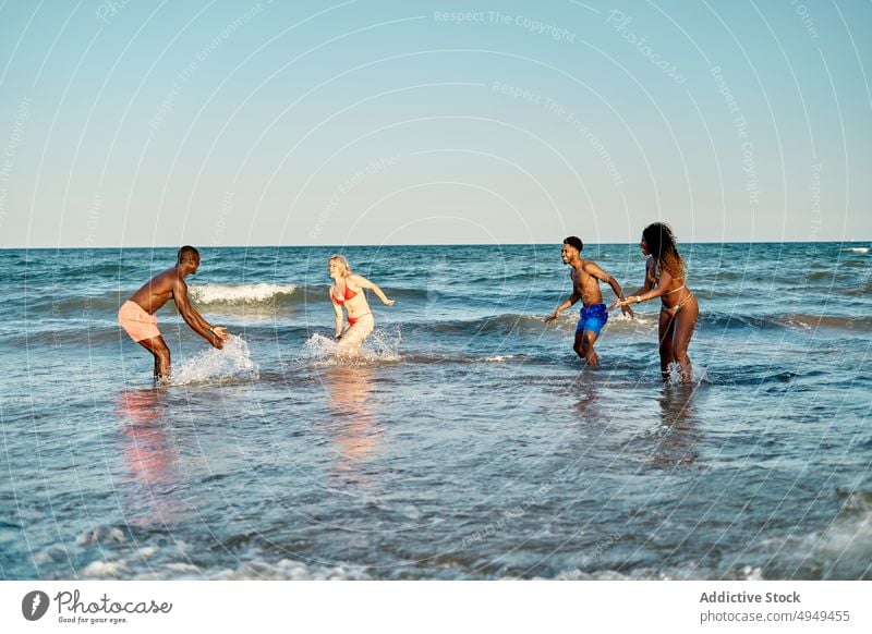 Multiracial friends playing in sea water summer weekend splash beach together wave men women diverse multiracial multiethnic black african american swimsuit