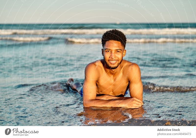 African American male lying near sea man beach wave summer weekend sand tourist wet water coast vacation ocean holiday shore daytime shirtless curly hair