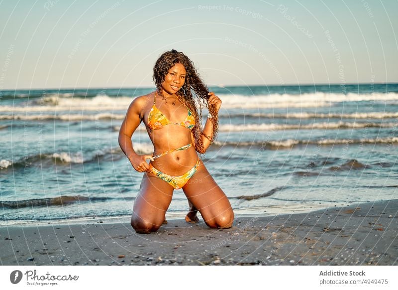 African American woman kneeling near sea beach weekend touch hair summer sunset vacation resort female holiday black african american ethnic bikini wave tourist