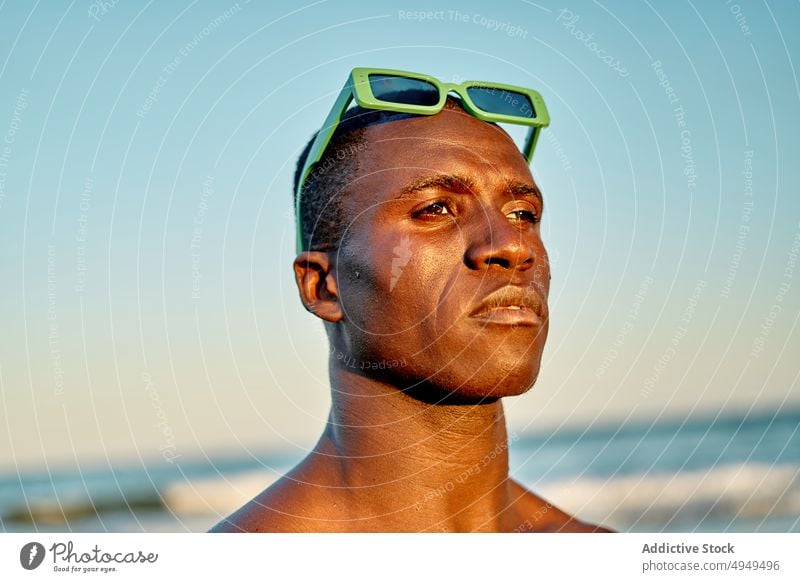 Serious black man near sea at sunset beach vacation serious weekend cloudless sky sunglasses portrait male african american ethnic summer calm sundown accessory
