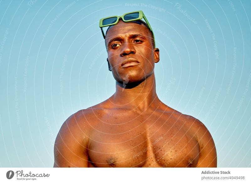 Serious black man near sea at sunset beach vacation serious weekend cloudless sky sunglasses portrait male african american ethnic shirtless summer calm sundown