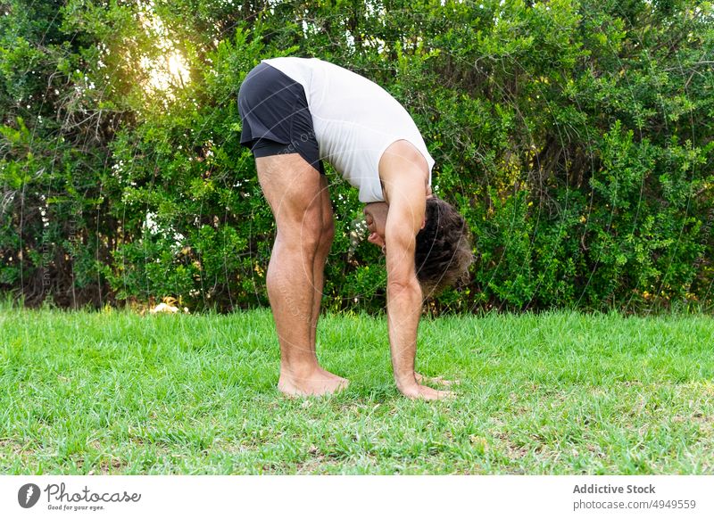 Flexible man doing Standing Forward Bend in park yoga session grass touch standing forward bend stretch practice flexible bush male barefoot lawn wellness
