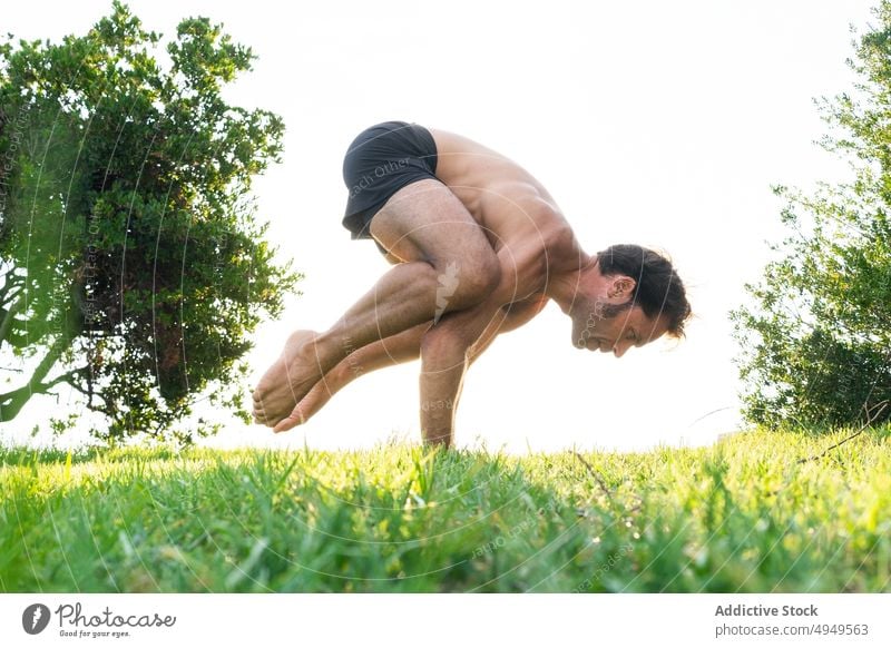 Mature man doing Crow pose on grass yoga balance practice summer lawn crow pose asana barefoot male wellbeing stretch energy zen peaceful wellness activity