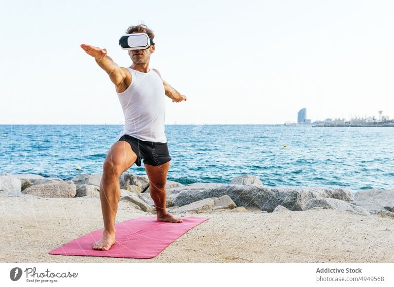 Man in VR glasses doing Warrior pose man yoga session beach sea vr headset warrior pose practice balance male backbend arm raised zen shore wellbeing wellness
