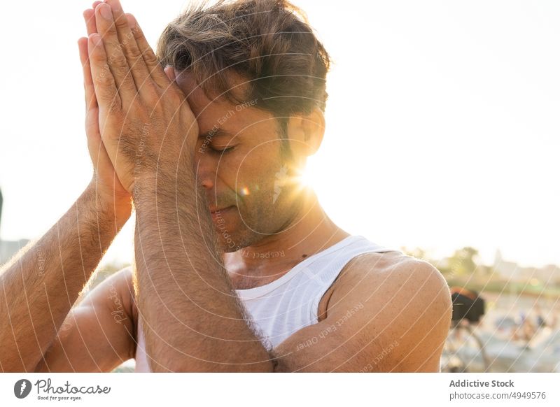 Middle aged male meditating in sunny morning man meditate session yoga beach third eye chakra hands clasped calm sunrise practice mature middle age