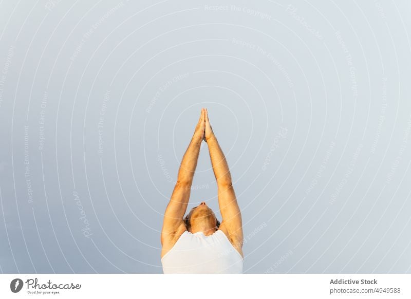 Cropped male doing Vriksasana pose against gray sky man yoga practice balance tree pose summer zen daytime wellbeing energy arms raised wellness mature activity