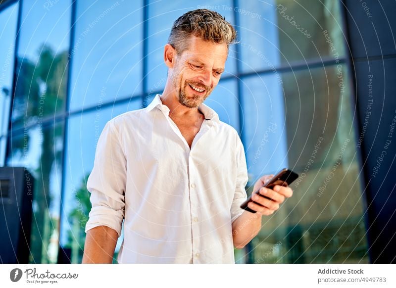 Businessman using smartphone near glass wall businessman street smile social media happy manager browsing building urban male middle age mature internet online
