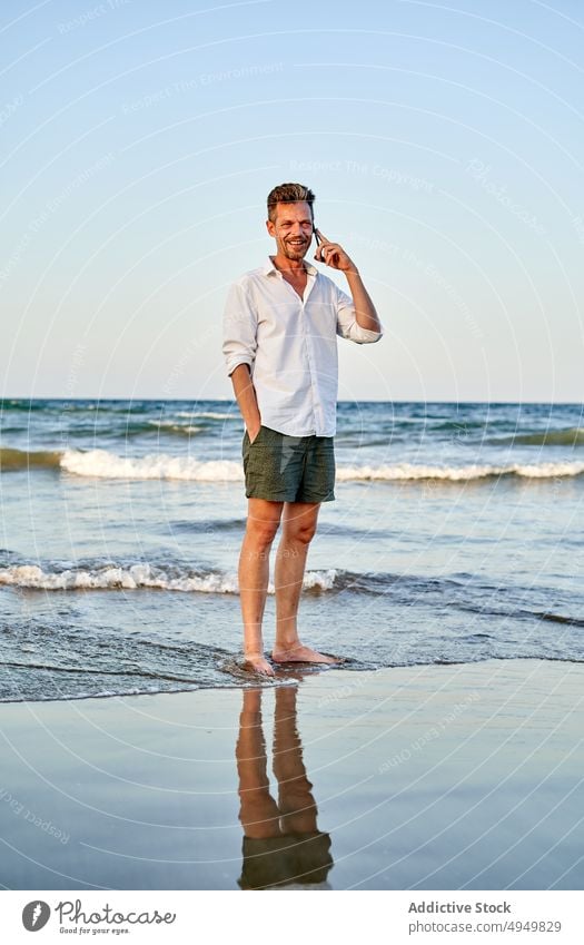 Businessman walking near sea and talking on smartphone businessman smile using vacation beach summer phone call telework male barefoot coast conversation happy