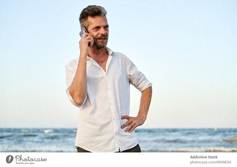 Businessman walking near sea and talking on smartphone businessman smile using vacation beach summer phone call telework male coast conversation happy device