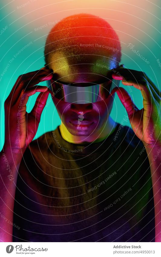 Serious young ethnic man touching VR glasses in neon studio virtual reality explore futuristic immerse cool digital experience adjust vr goggles male
