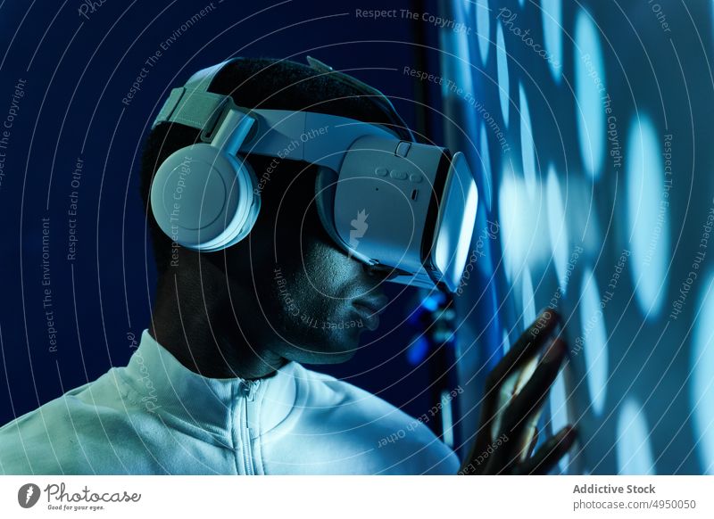 Serious black man touching large screen while exploring virtual reality in modern headset touch screen interact explore futuristic vr neon cyberspace entertain