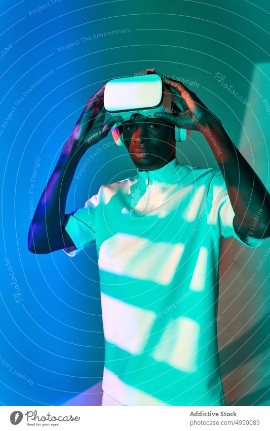 Cool young African American adjusting VR goggles in studio man virtual reality take off experience futuristic vr serious portrait innovation digital