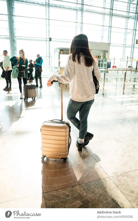 Anonymous woman in airport terminal traveler suitcase lean wait trip passenger departure female baggage vacation dark hair tourism tourist daylight sunlight