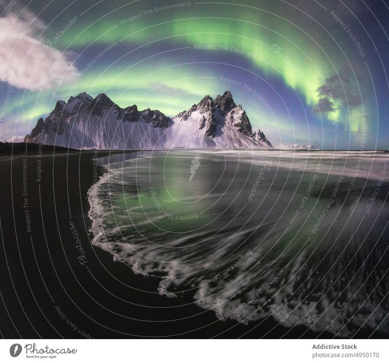 Water and snowy mountain against polar lights water sky aurora night peak shore winter calm vestrahorn iceland coast nature lake weather picturesque