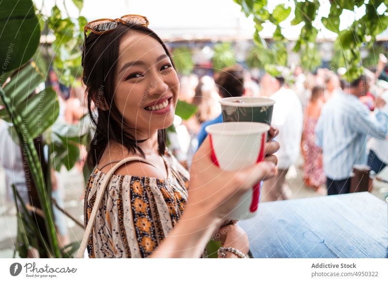 Happy Asian woman proposing toast to friend clink paper cup soft drink restaurant smile weekend street seville spain female asian ethnic together spend time