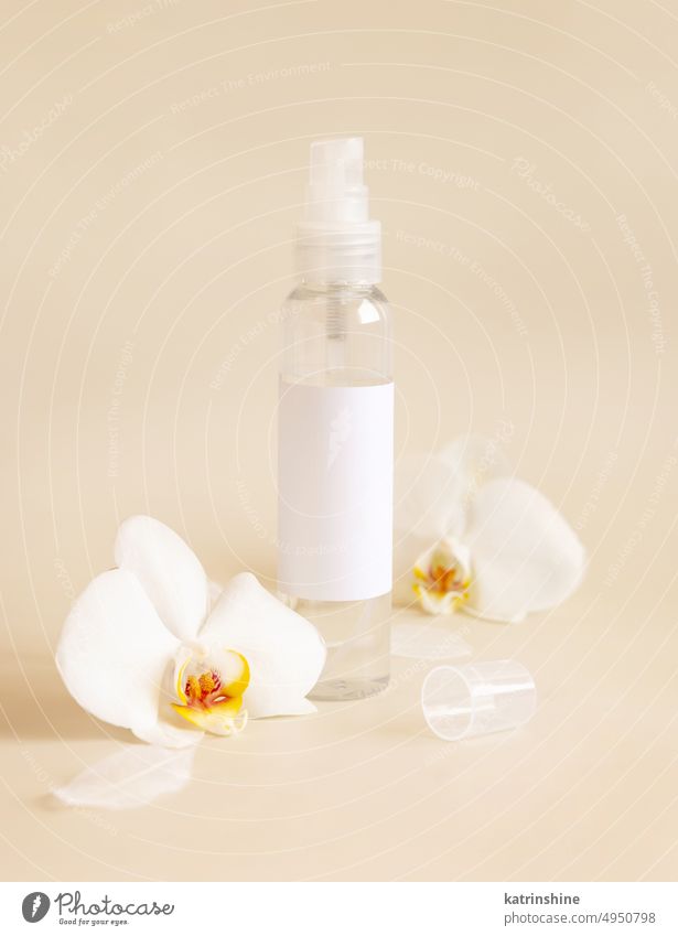 Spray dispenser bottle near white orchid flowers on light beige close up. Mockup mockup tropical label pastel negative space copy space top view Brand package