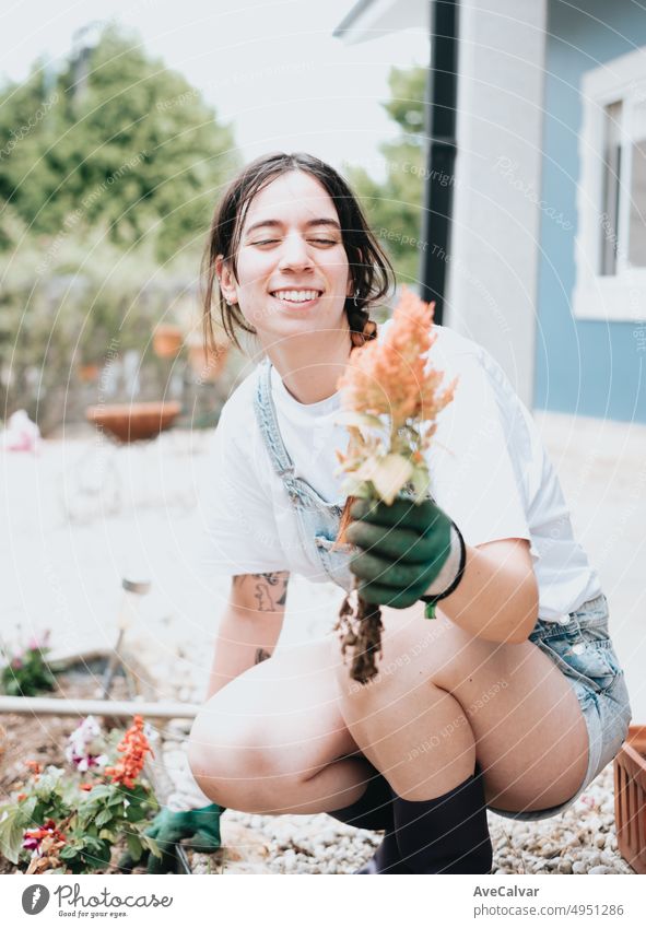 Cheerful young woman in gloves using gardening tools for planting flowers on back yard.in casual clothes enjoying work at summer garden. Home garden new skills learning.Concept of gardening and floristics