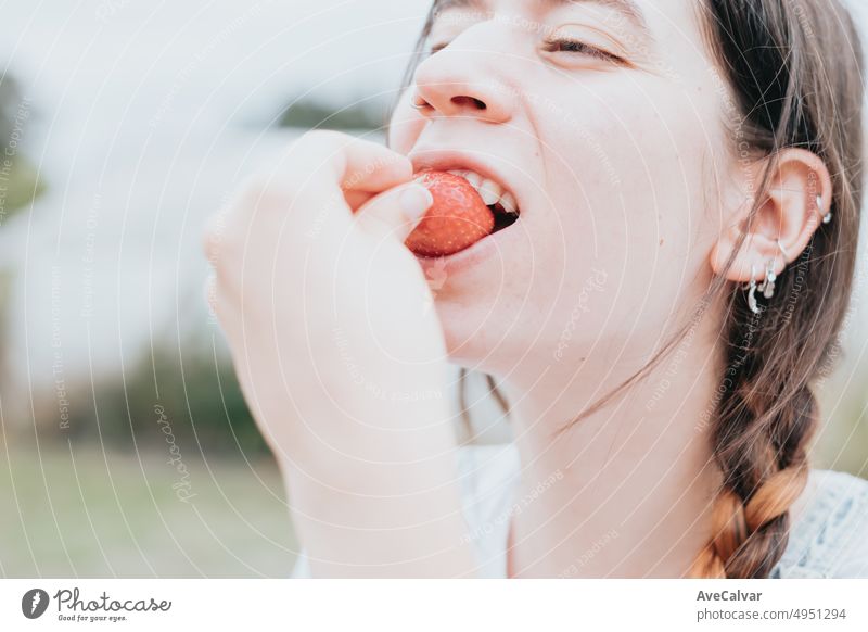 Positive woman farm worker tasting harvested strawberry, working in greenhouse. Healthy lifestyle and healthy eating.Fruit and berries Female farmer with strawberry crop. Smiling woman holding straws