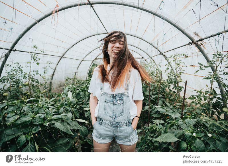 Young woman waving hair standing in greenhouse near plants with vegetables. Sustainability and responsible growing concept. Eco and bio healthy food harvesting.