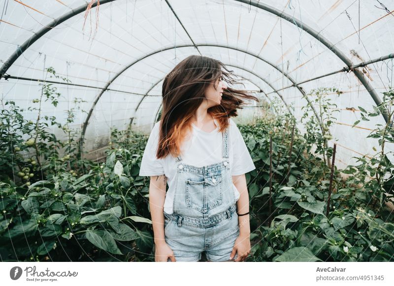 Young woman waving hair standing in greenhouse near plants with vegetables. Sustainability and responsible growing concept. Eco and bio healthy food harvesting.