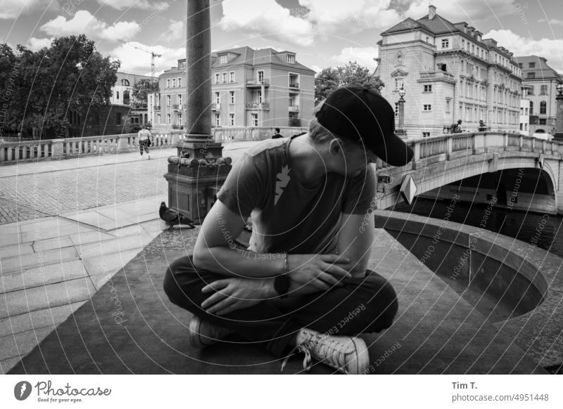 a young man with cap looks down sitting Berlin Middle Spree Bridge b/w Man Baseball cap bnw Exterior shot Day Black & white photo Capital city Downtown Town