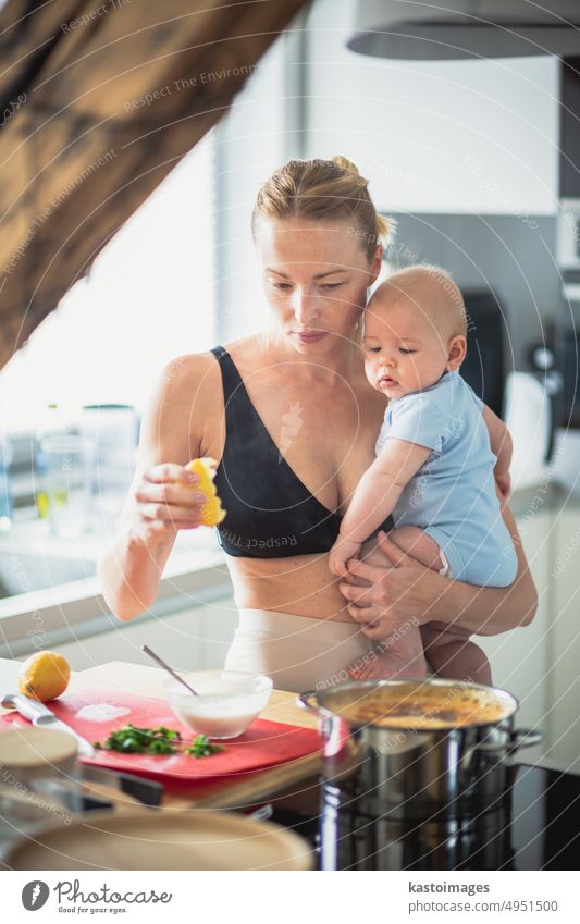 Woman cooking while holding four months old baby boy in her hands. childhood family motherhood woman parent kitchen home son busy food learning development kid