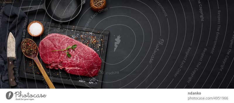 Raw beef tenderloin lies on a brown wooden board, black table. meat uncooked raw slice spice butcher cow fillet barbecue beefsteak top nobody preparation