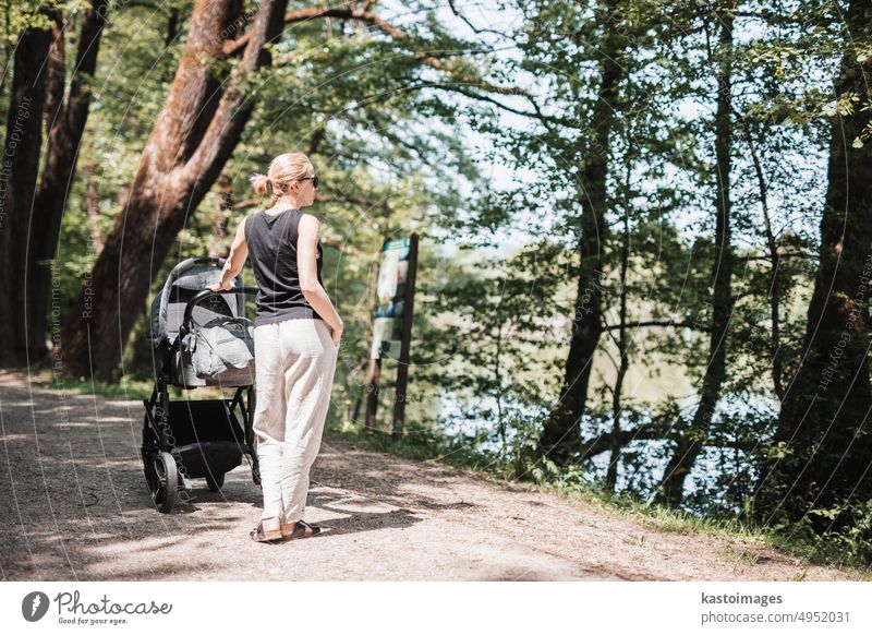 Rear view of casualy dressed mother walking with baby stroller in city park. Family, child and parenthood concept. family motherhood nature lifestyle pram