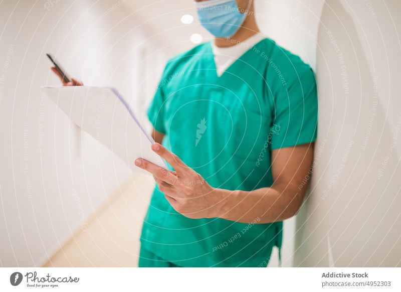 Doctor with papers in hospital corridor doctor read uniform professional job sterile attentive man surgeon light lamp shiny focus medic mask protective green
