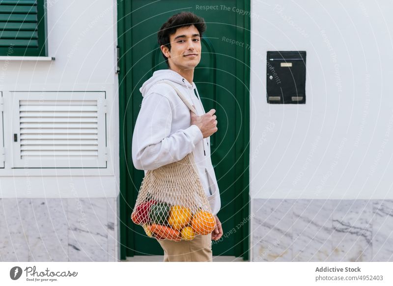 Man with fruits in mesh bag in city man eco friendly street grocery natural zero waste male organic cheerful smile urban ripe fresh shopper shopping bag happy