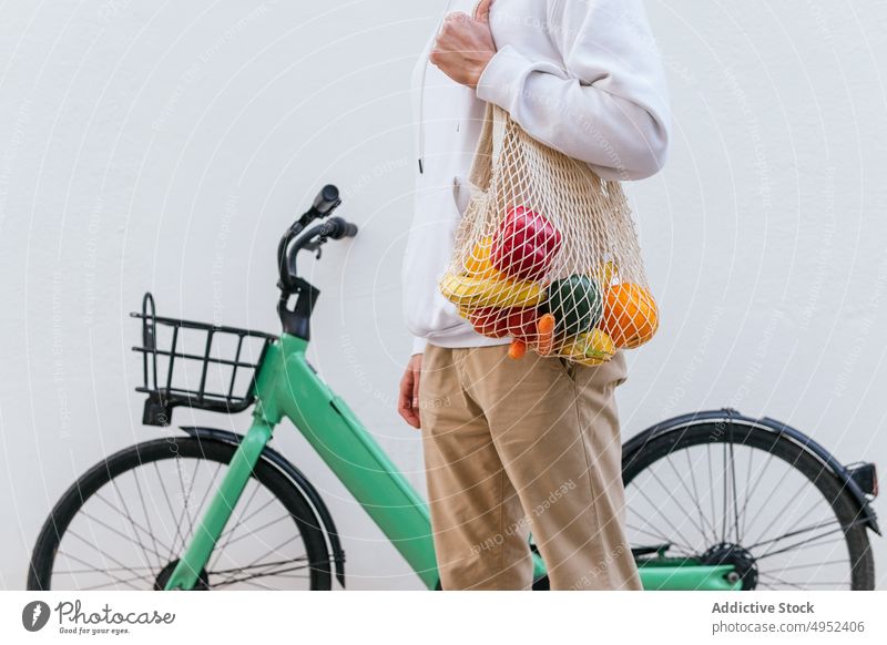 Crop man with mesh bag standing near bicycle in city grocery eco friendly zero waste street natural shopping bag male bike modern transport fruit vegetable