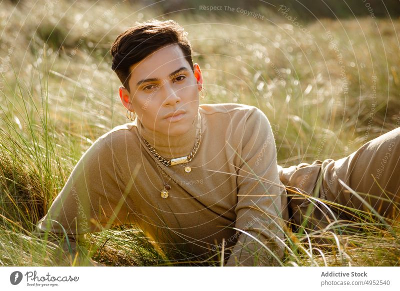 Trendy ethnic guy resting in field man grass countryside style outfit summer portrait model male sunny daytime casual accessory fancy trendy lying young relax