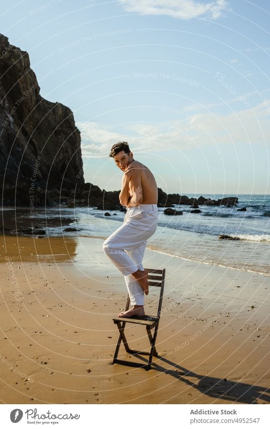 Shirtless man standing on chair near sea beach style balance concept vulnerable embrace male model young shirtless barefoot coast shore ocean summer water guy
