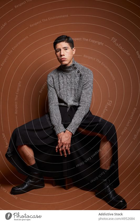 Stylish homosexual model in sweater on brown background gay fashion style hands clasped feminine lgbt man unemotional portrait knitted cloth boot leather